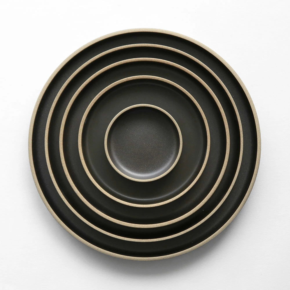 A set of five nested round ceramic plates in matte black with a contrasting light beige rim, photographed from directly above on a clean white background.