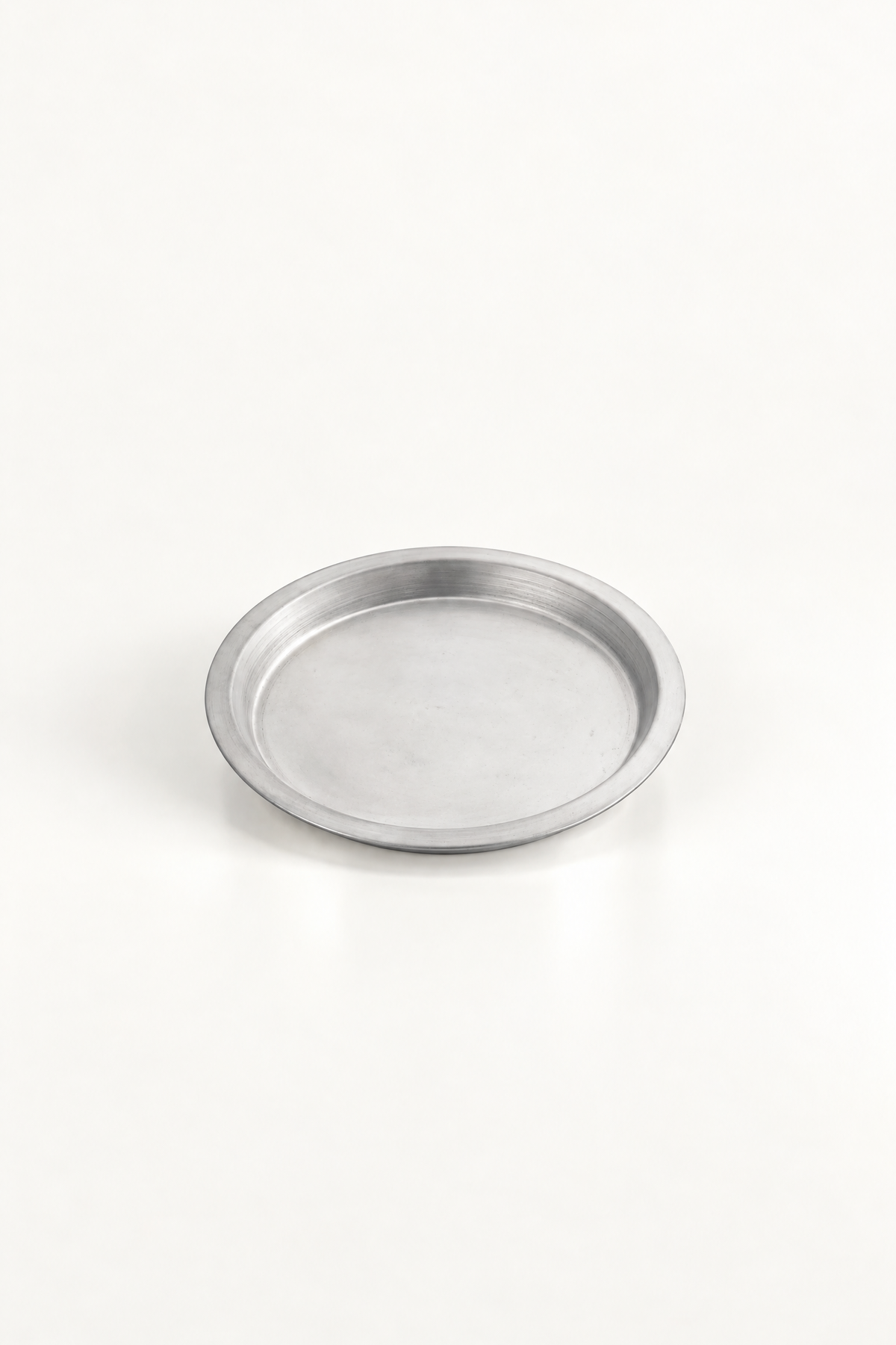 A small round metal tray with a shallow depth of field, photographed on a seamless white background.